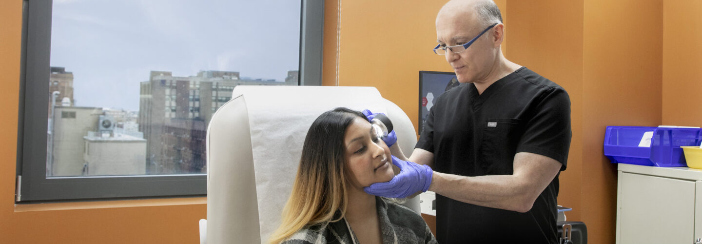 Dr. Daniel Buchen performs dermatology exam using dermatoscope for female patient in exam room