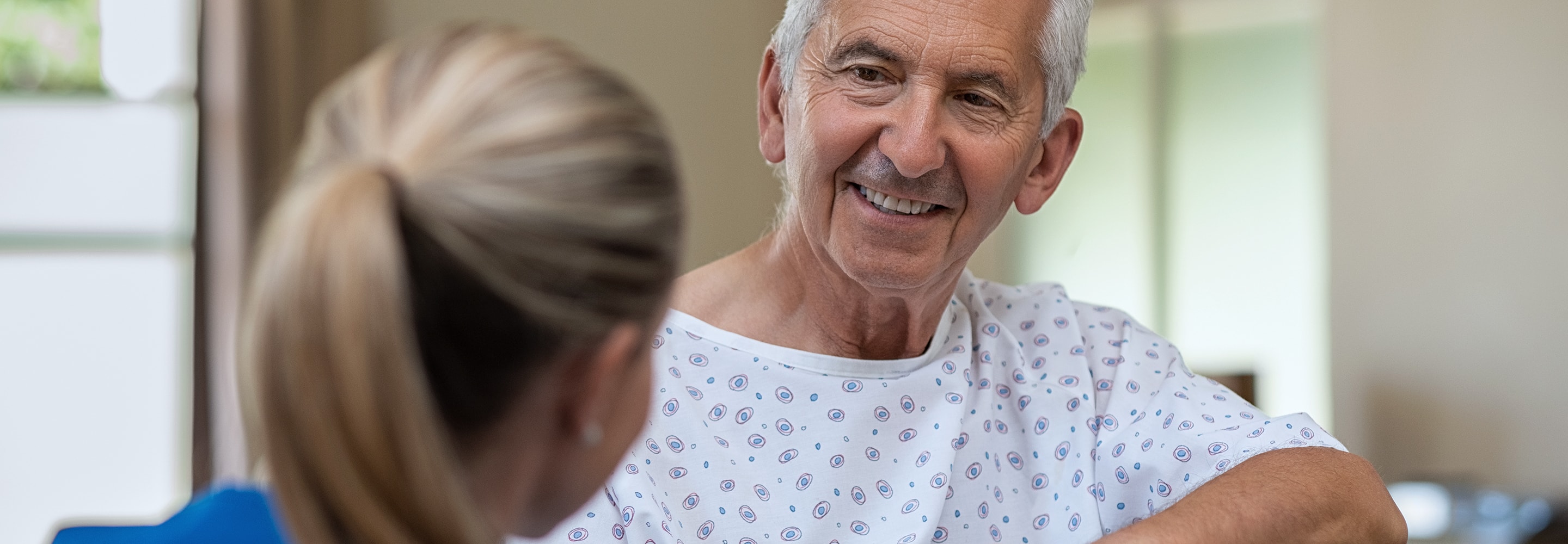 Older male patient in hospital gown talking to nurse