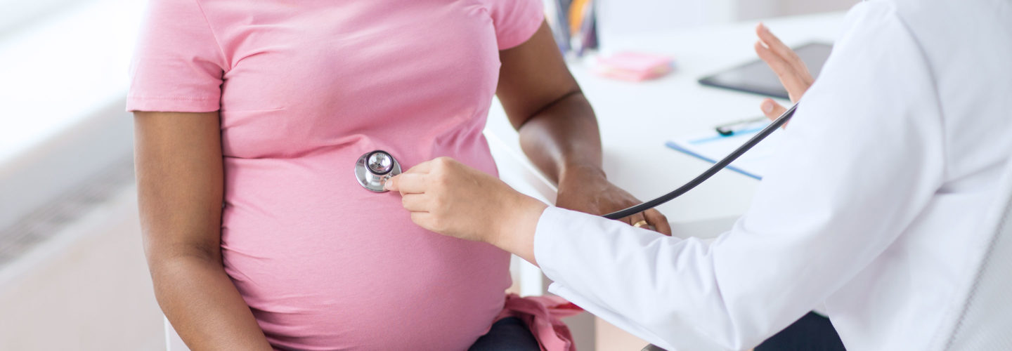 Doctor listens with stethoscope during examination of pregnant woman