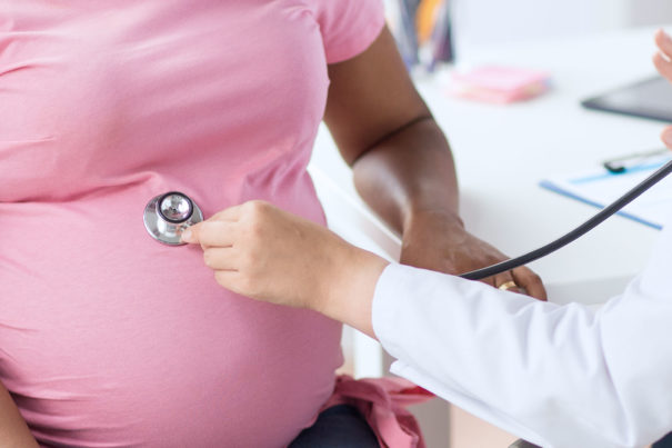 Doctor listens with stethoscope during examination of pregnant woman