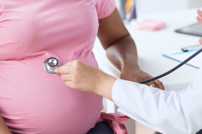 Doctor listens with stethoscope during examination of pregnant woman