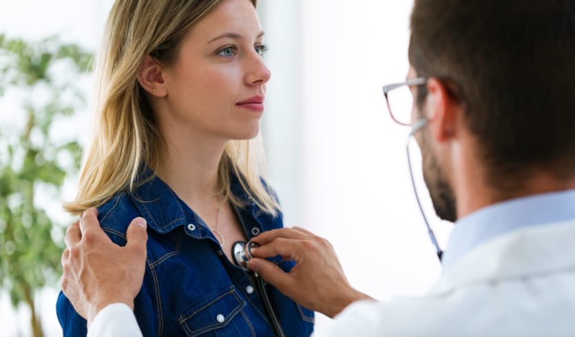 Doctor listens to woman's heart with stethoscope