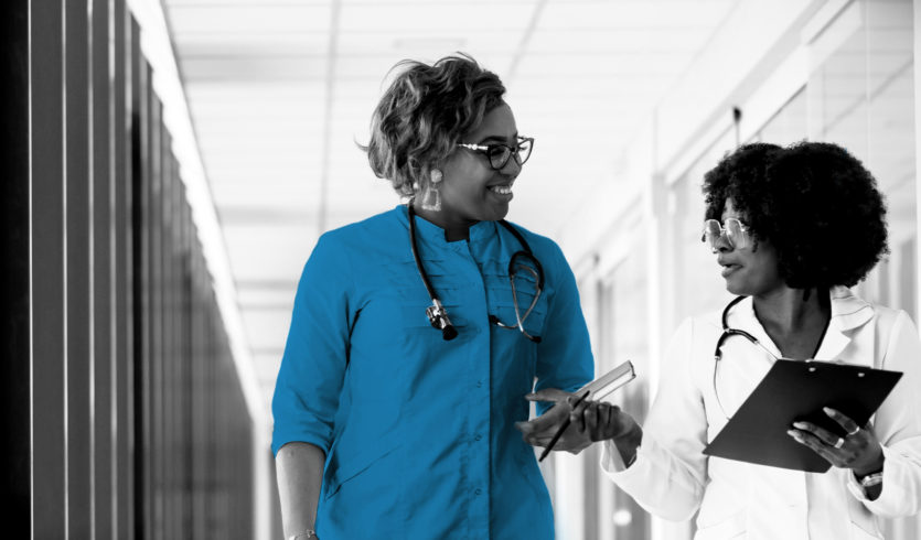 A doctor and nurse speak as they walk down a hallway