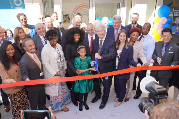 Child holds large scissors to cut ribbon, surrounded by large crowd