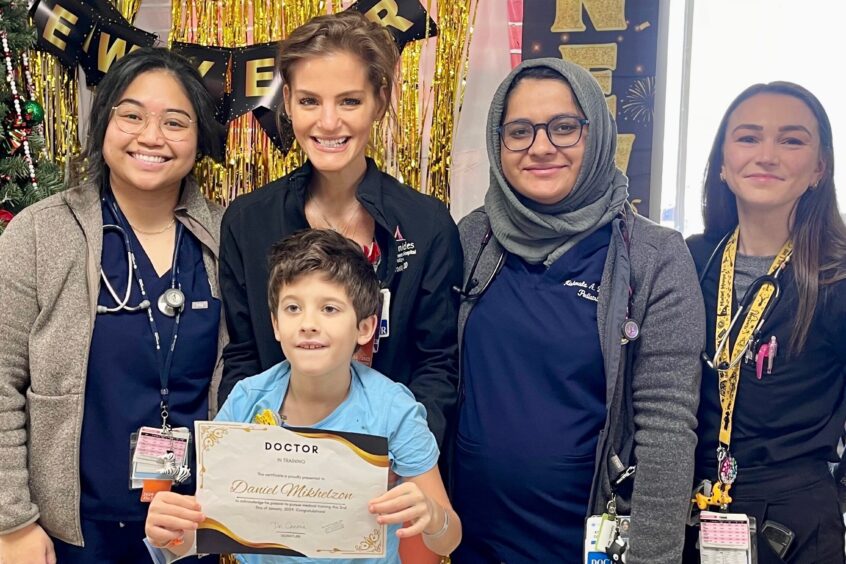 Daniel holds doctor-in-training certificate in front of his care team; new year's decorations are in the background