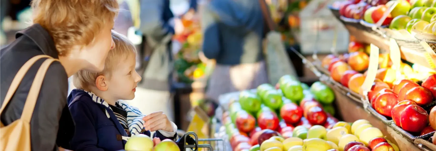 Mother with son in a shopping cart looking at an assortment of apples in a grocery store