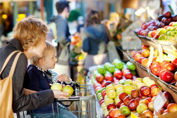 Mother with son in a shopping cart looking at an assortment of apples in a grocery store